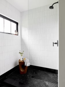 A modern bathroom with white tiled walls and black hexagonal floor tiles, featuring a shower stall.
