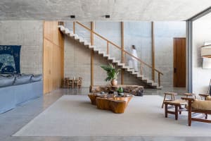 Modern living room with concrete walls, wooden furniture, and a large staircase.