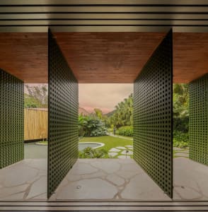Modern residential entryway featuring green metal perforated panels and natural stone flooring.
