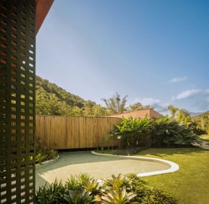 Modern house exterior with wood fences and a curved pool surrounded by greenery and trees.