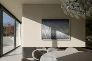 A minimalist dining area featuring glass and metal furniture, fabric upholstery, and a large window with views of nature.
