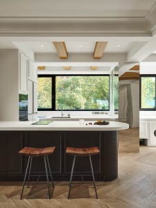 A modern kitchen featuring a marble countertop with wood stools and stainless steel appliances, surrounded by wood flooring a