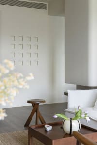 A modern minimalist living room with neutral tones, featuring a white sofa, wooden stool, and decorative vase with tulips.