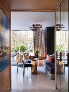 Modern dining room featuring a round wooden table with a geometric gold base, surrounded by black and woven chairs, and adorn