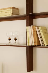 A modern bookshelf made of wood with books and wine glasses.