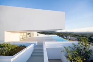 A modern residential architecture featuring a concrete structure and infinity pool overlooking scenic landscape.