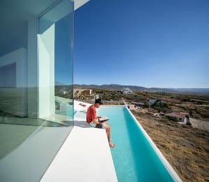 A modern minimalist house with a glass exterior overlooking a scenic landscape.