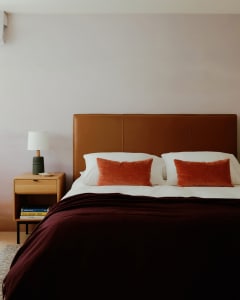 A minimalist bedroom with a brown leather headboard, orange cushions, and dark bedding.