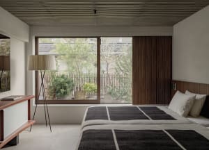 A minimalist bedroom with a large window, natural lighting, and a wooden headboard.
