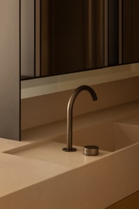 Modern minimalist bathroom featuring a sleek metal faucet mounted on a flat sink surface, set against a warm, neutral-colored