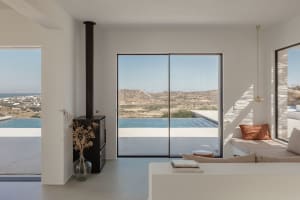 Modern minimalist living room with large windows overlooking the mountains and sea, featuring sleek concrete finishes and sim