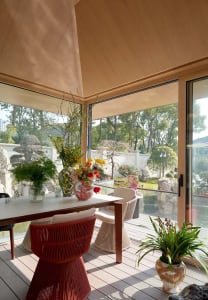 A modern patio with a wooden table, red chair, and flower arrangements in vases.