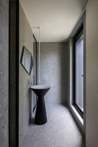 A modern bathroom with a minimalist design featuring concrete flooring and a black pedestal sink.