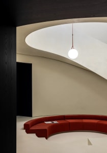 A modern lobby with a curved concrete seating area and a spherical light fixture hanging from the ceiling.