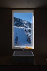 Modern bathroom with a concrete sink, yellow soap dish, white toothbrush, and a window overlooking a snow-covered mountain la