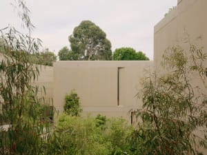 A minimalist architectural design featuring a modern exterior with concrete walls and greenery.