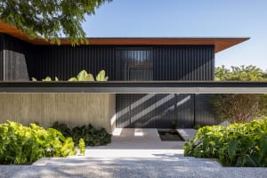 A modern house with a metal-clad exterior featuring a large window and greenery.