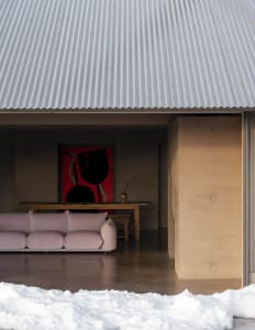 A modern living room with a pink fabric sofa, concrete walls, and a corrugated metal roof.