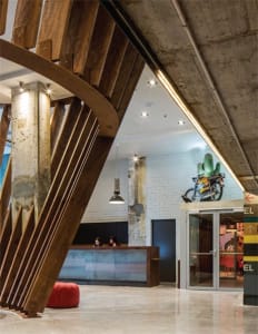 Modern industrial-style lobby featuring exposed concrete walls and wooden beams, with a reception desk and seating area.