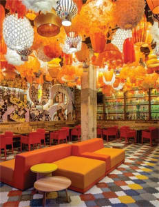 A brightly lit interior of a modern restaurant with hanging fabric decorations and glass and metal elements.