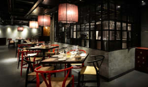 A contemporary dining room with red and black furniture, wooden chairs, and concrete walls.