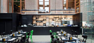 A modern restaurant interior featuring black and green accents, with a bar, tables, chairs, and a glass display case.
