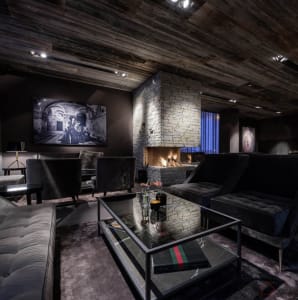 A dark, industrial-style living room with wooden ceiling, stone fireplace, and modern furniture.
