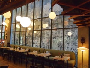 Modern restaurant interior with large windows, bench seating, and hanging spherical lights.
