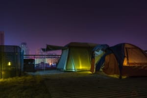 Tents set up at night on a rooftop with a view of the city skyline.