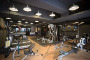 A modern, industrial-style fitness center with metallic equipment and laminate flooring.