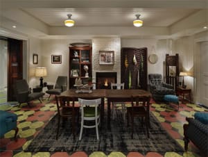 A cozy, industrial-style living room with a fireplace, wooden table, chairs, and a patterned rug.
