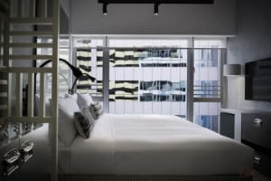 Clean, modern bedroom with a minimalist aesthetic, featuring a sleek bed with white bedding, and a large window offering city