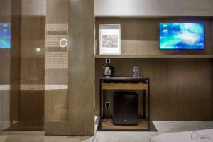 A modern minimalist hotel room with wooden accents, glass partitions, and metallic furniture.