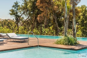 A modern residential pool with a wooden deck and glass surroundings.
