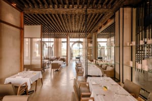 Modern restaurant interior with industrial-style decor featuring wooden ceiling, glass shelves, and concrete flooring.