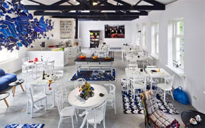 Industrial-style cafe interior with concrete and metal elements, featuring white tables and chairs.