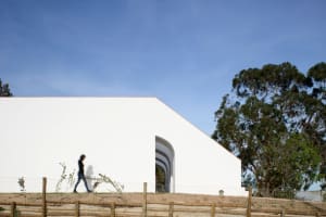 A modern residential building with a white concrete exterior, features large windows and an open archway, set against a clear