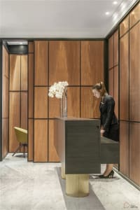 A modern hotel reception area with a wooden desk, glass vase with white flowers, and marble flooring.