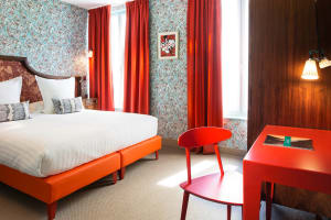 A minimalist bedroom featuring bright orange furniture and red-orange patterned curtains with a framed picture on the wall.