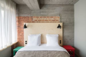 Modern, industrial-style bedroom with concrete walls and a wooden bed headboard, featuring white pillows and a textured bedsp