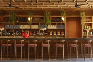 A modern industrial restaurant bar with wooden seating, glass shelves, and metal fans.