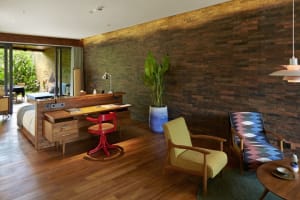 A modern bedroom with a wooden desk, brick accent wall, and tropical plant.