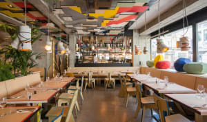Modern restaurant interior with colorful geometric shapes, concrete and wood materials, and industrial design elements.