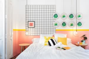 A modern bedroom with a white bed, vibrant accents, and geometric grid design on the wall.