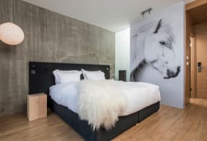 Modern minimalist bedroom featuring a black bed with white bedding, a white fur throw, and a large black and white horse wall