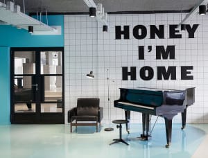Modern interior with white tiles, black accents, and a black grand piano with text 'Honey I'm Home'.