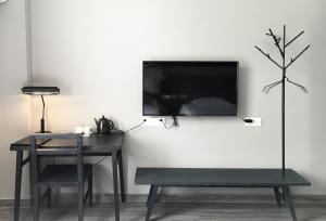 A minimalistic hotel room with a black desk, black bench, and a mounted television on the wall.