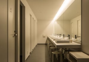 Modern white ceramic public toilets with sinks and mirrors.