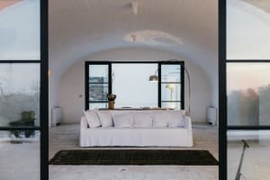 A cozy living room with a white concrete sofa, large windows, and a comfortable rug.