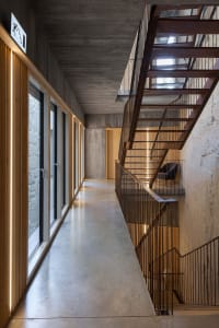 Industrial-style office corridor with concrete floor, wooden panels, and metal stairway.